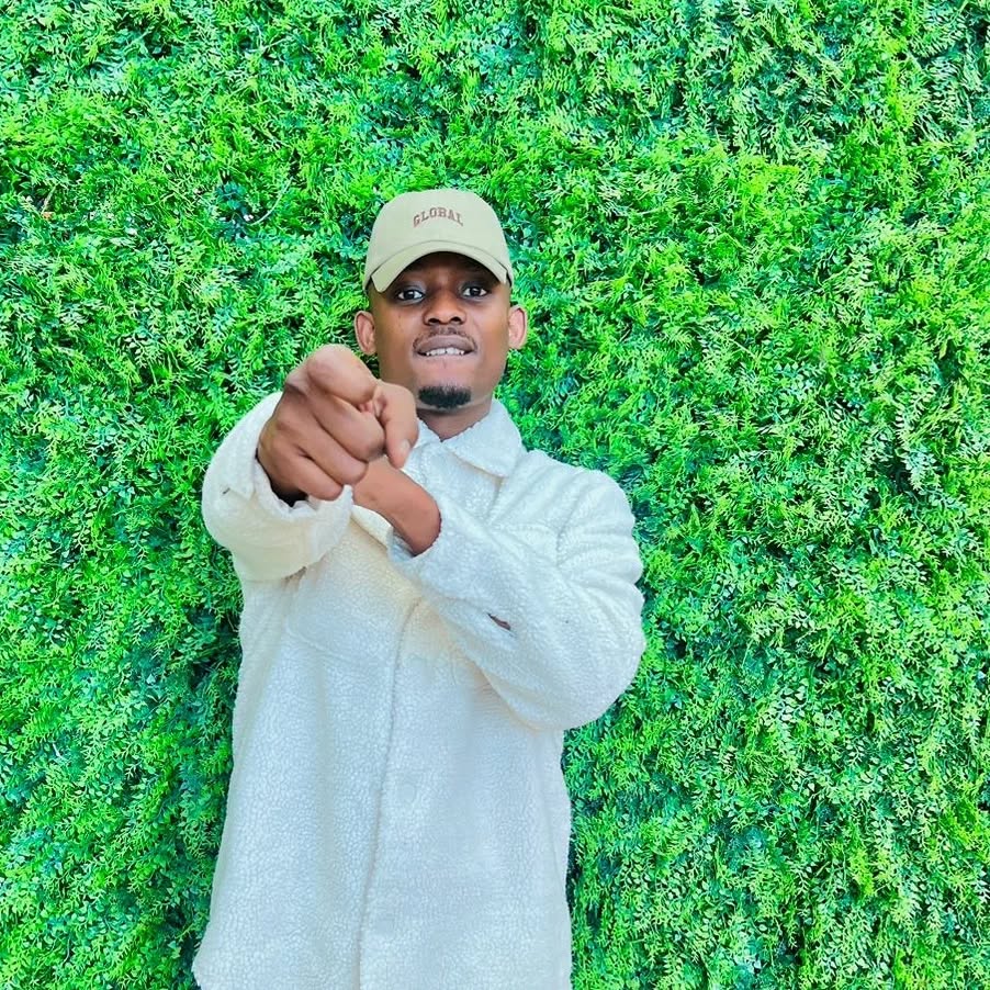 Gino Batyashe - South African hip-hop artist and entrepreneur, pointing confidently at the camera with a vibrant green foliage background